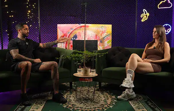 Relaxed podcast studio setup with two people in conversation, modern decor, and vibrant neon accents.