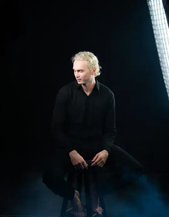 Contemporary man seated in a dark studio with professional lighting for portrait photography.