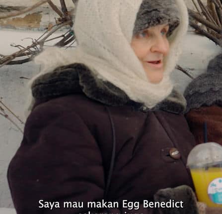 Woman in winter clothing outdoors, holding a snack in snowy landscape.
