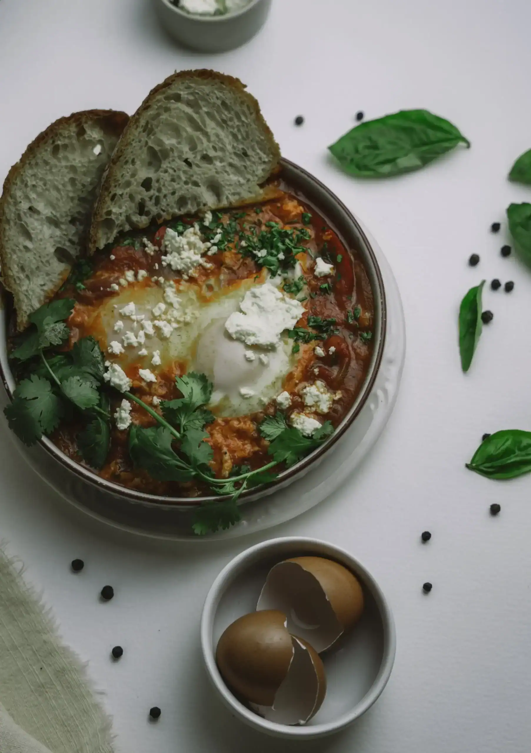 Savory baked eggs in tomato sauce with bread, herbs, and feta cheese, served for breakfast or brunch.