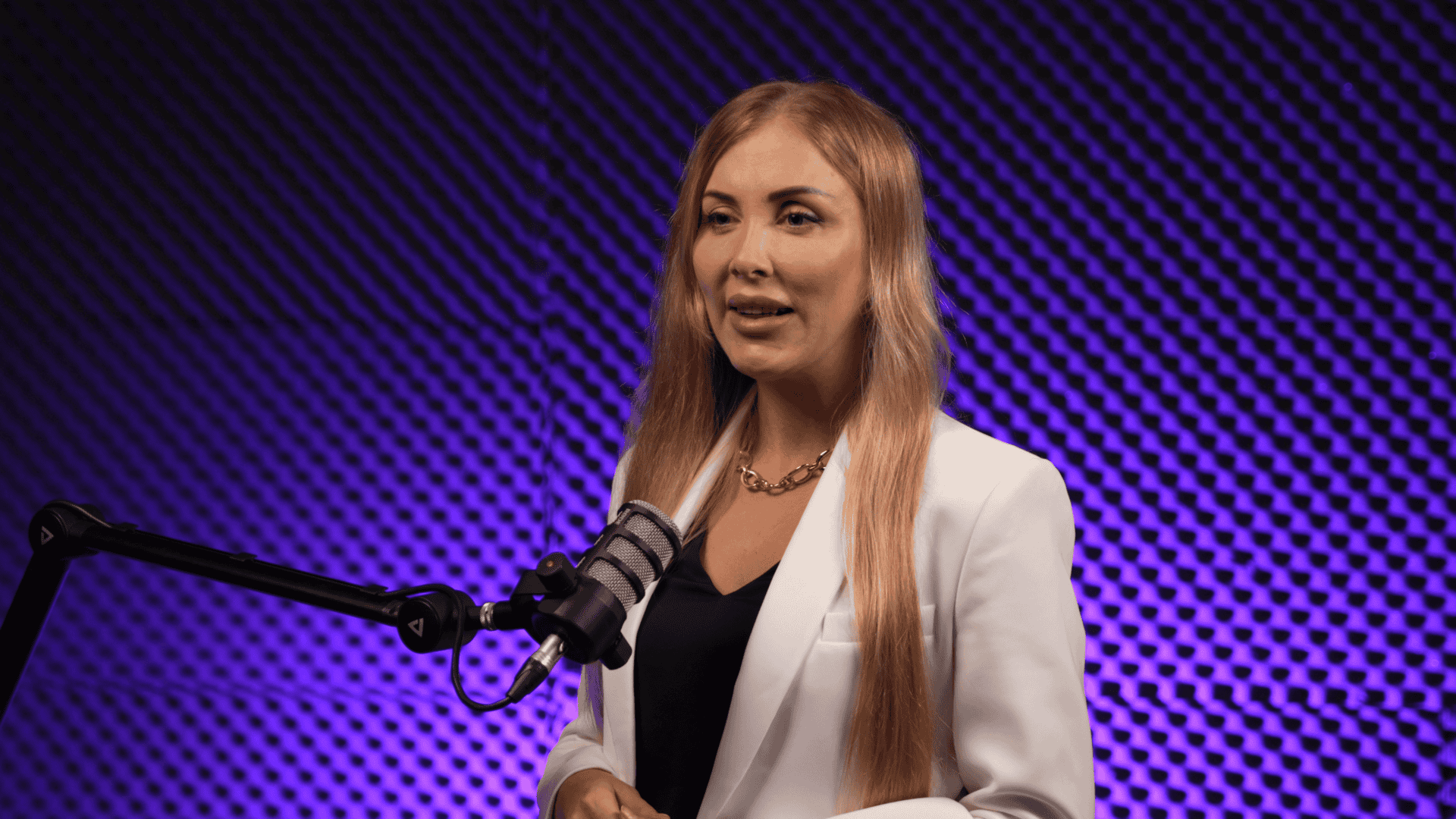 Elegant woman in white blazer speaking in podcast studio with purple soundproof background.