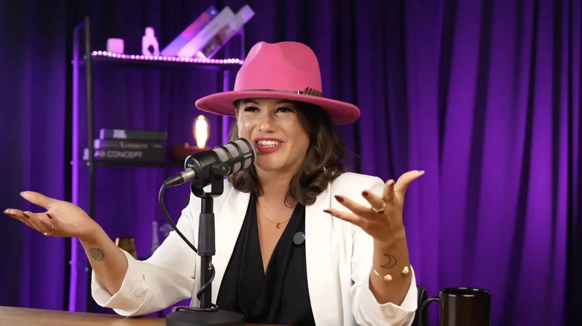 Vibrant podcast studio with a female host wearing a pink hat and white blazer, speaking into a microphone.